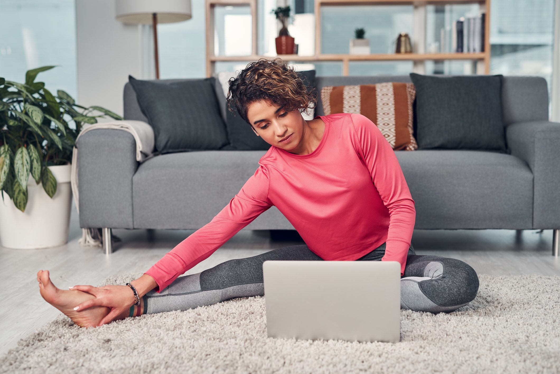 A woman sitting on the floor in athleisure with a laptop in her lap.