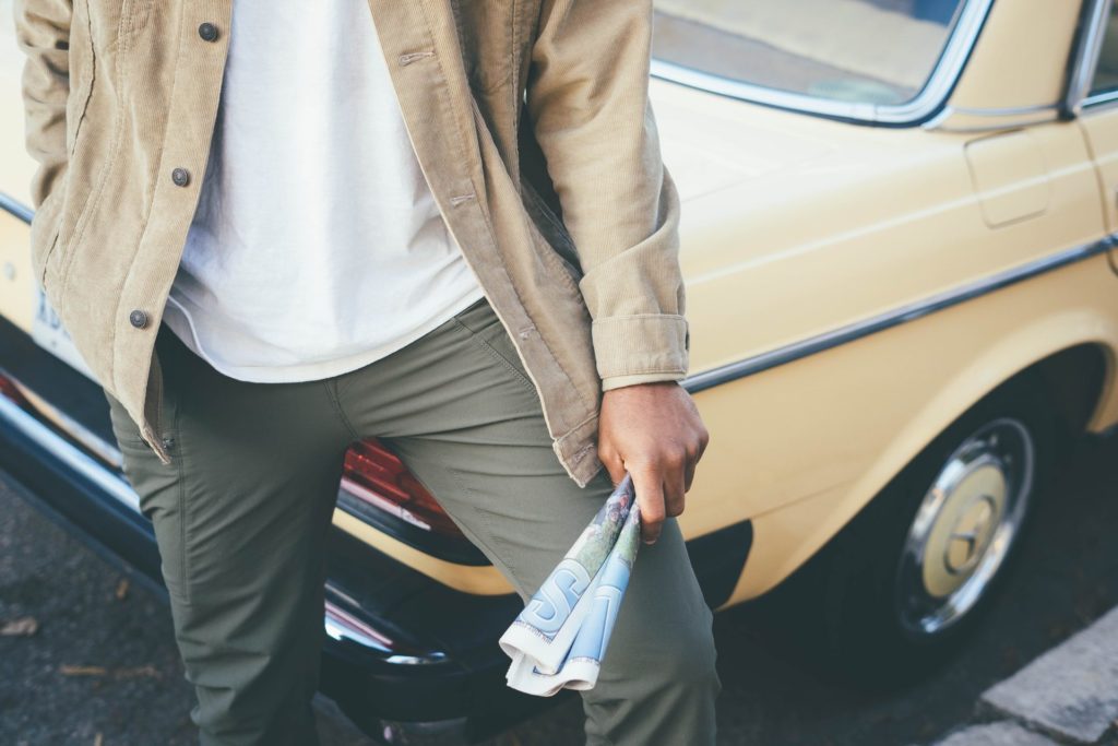 A man in athleisure attire standing next to a car holding a newspaper.