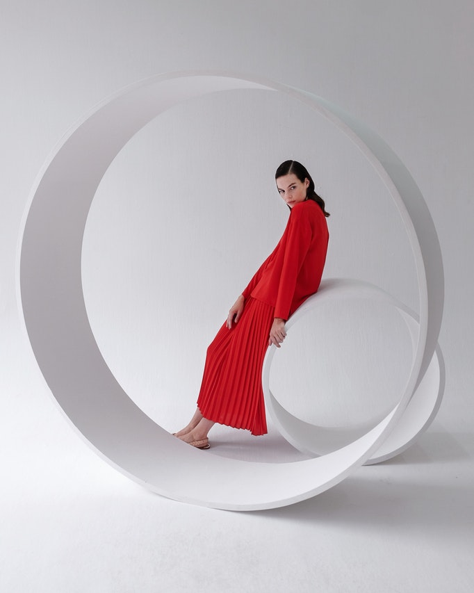 A woman in a red dress showcasing a clothing collection while sitting on a circular chair.
