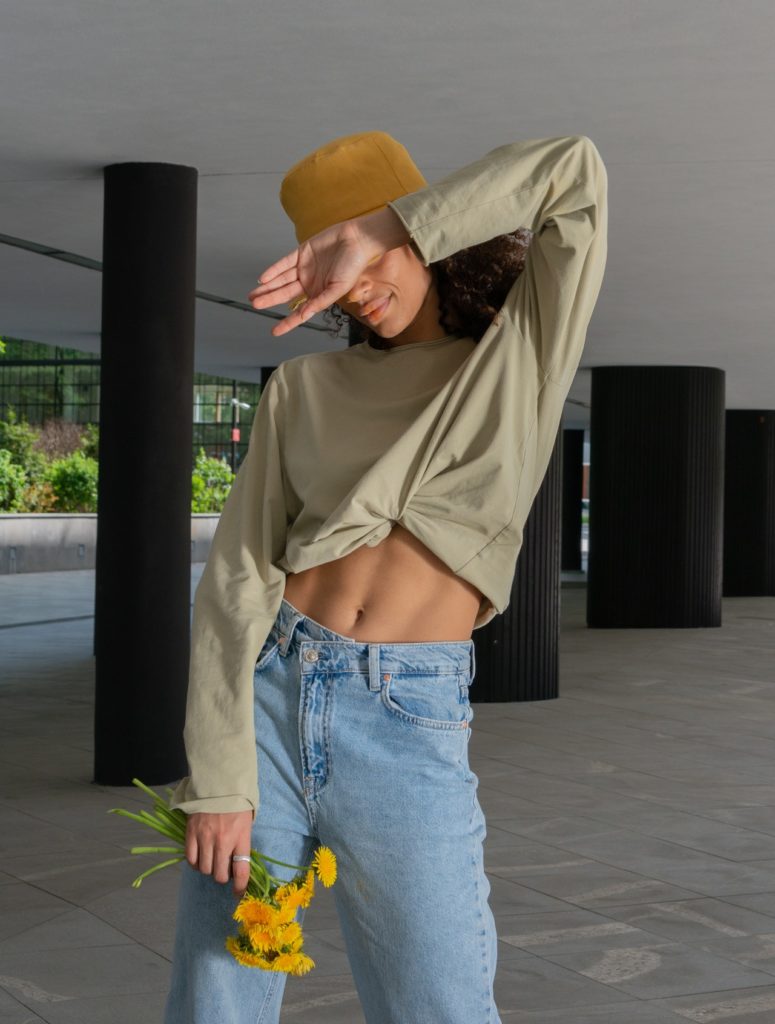 A woman in jeans and a hat strikes a pose for a photo, showcasing the latest addition to her clothing collection.