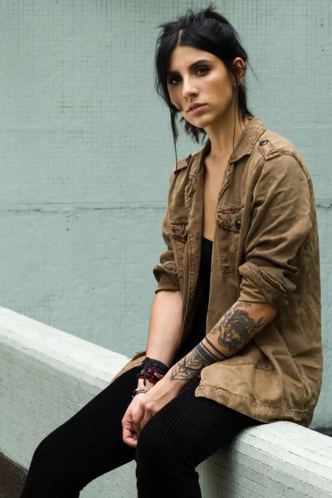 A woman with tattoos sitting on a wall wearing casual wear.